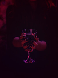 A woman in black robes presenting a chalice of liquid, as though part of a ritual.